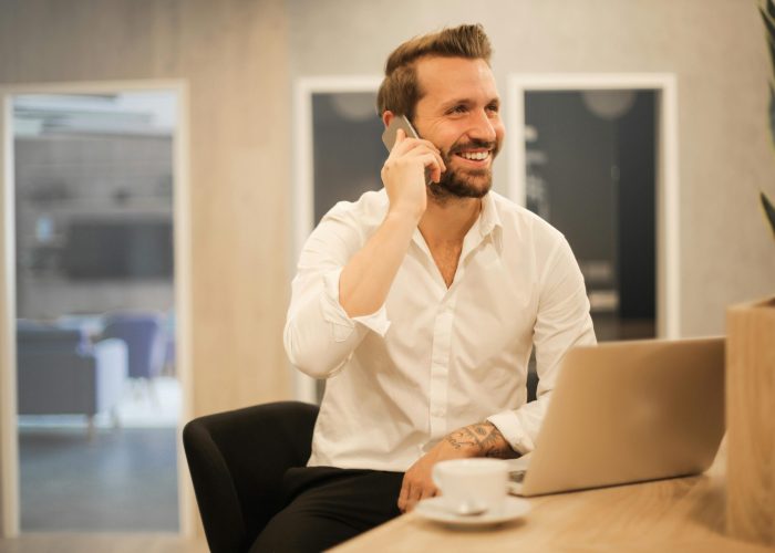 Happy businessman in white shirt on phone call at modern office desk with laptop.